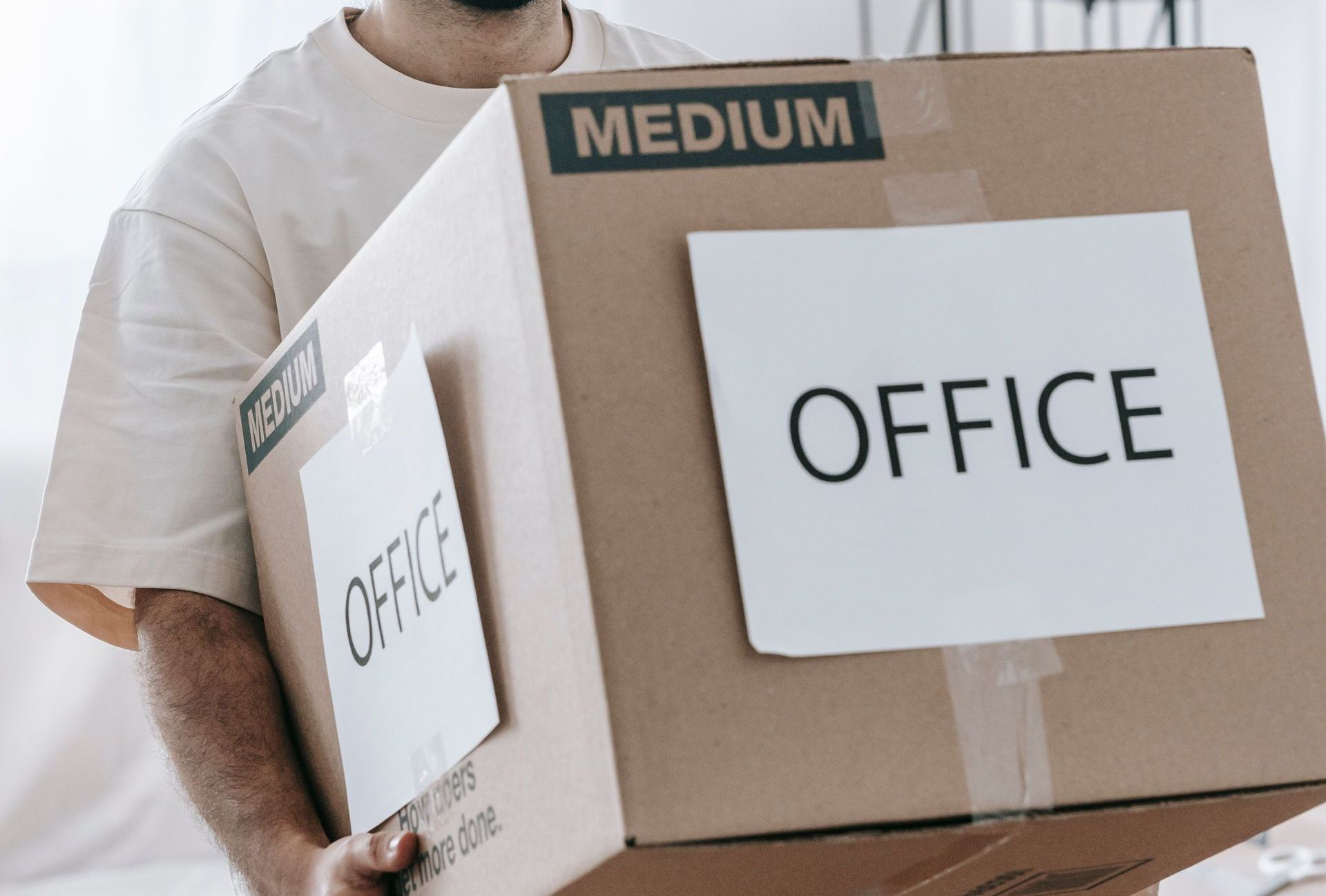 Man moving box labeled 'Office' indoors during relocation or packing.